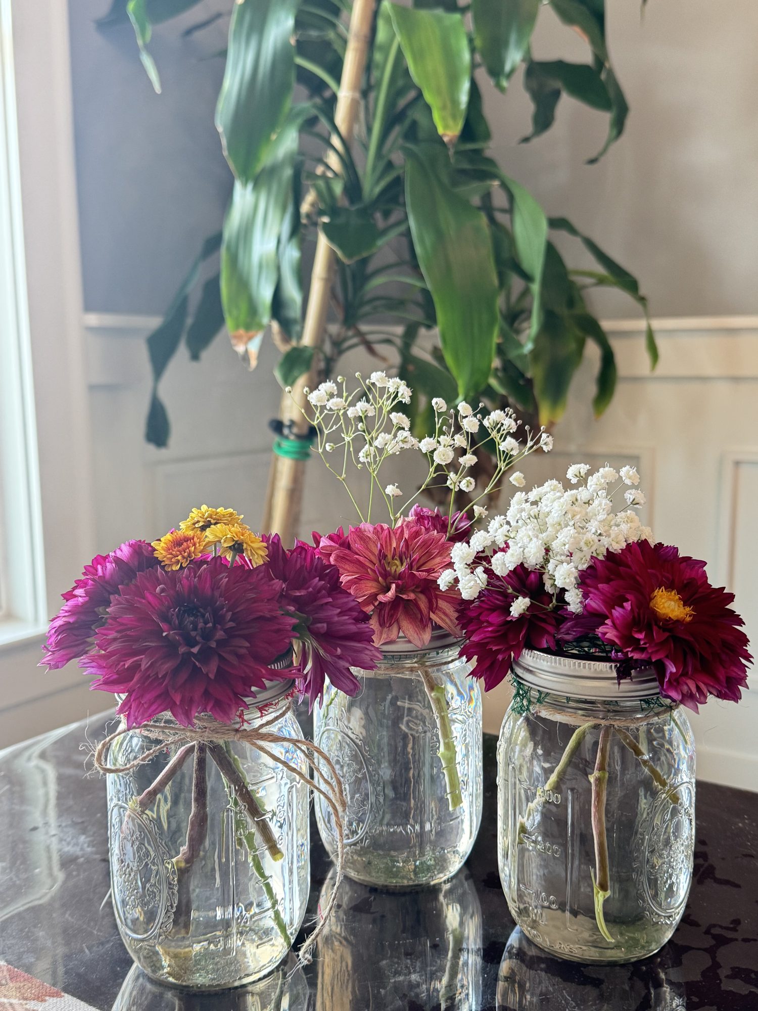 Three bouquets of dahlias and baby's breath in glass jars tied with twine.
