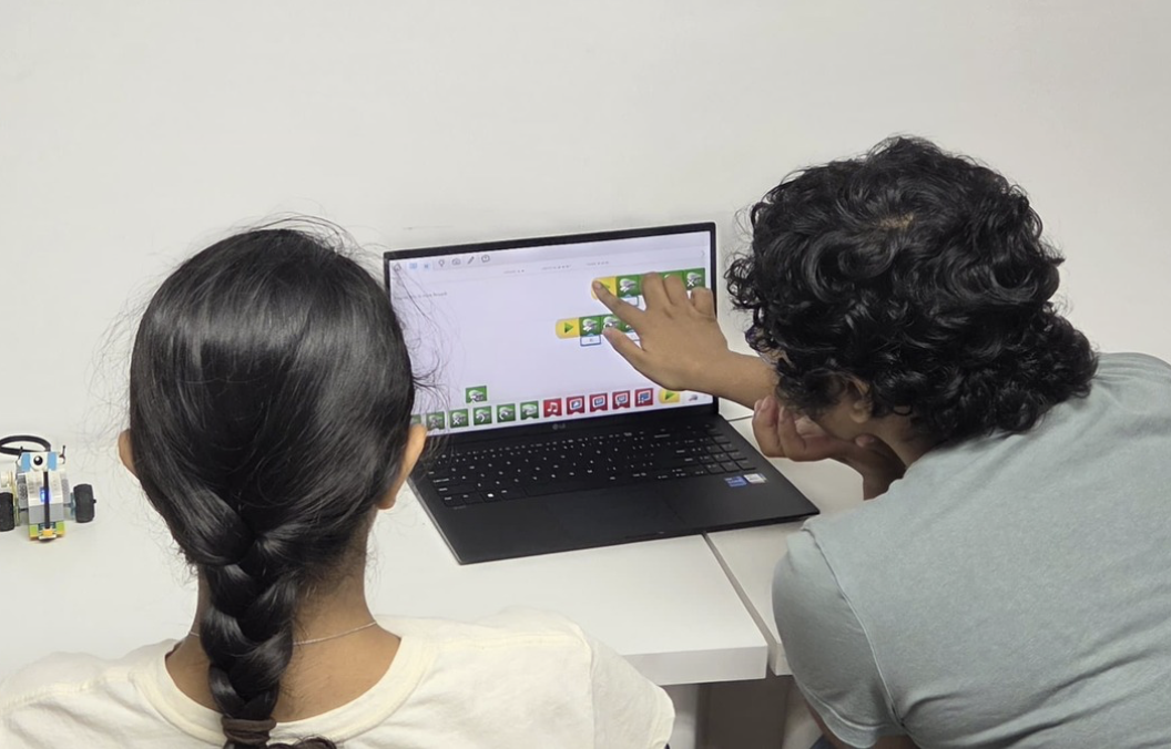 Two young people at a laptop, one pointing to blocks of code on the screen.
